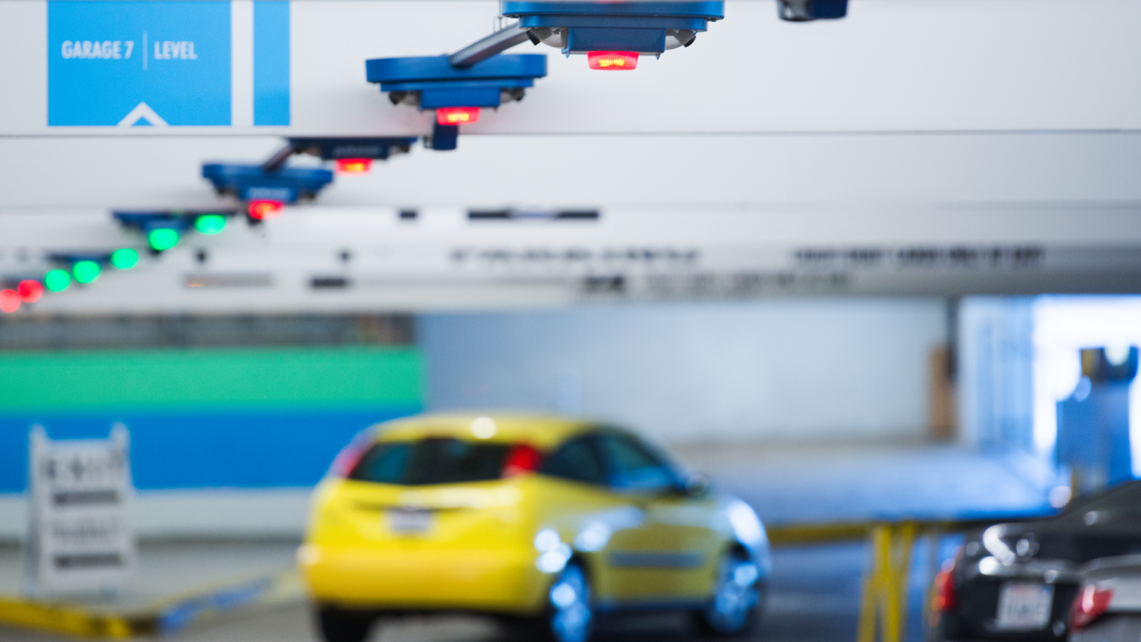 Een parkeergarage met een gele auto, sensoren boven de parkeerplaatsen met rode en groene lampjes, en een bord met de tekst 'Garage 7 Niveau'. Een parkeergarage met een gele auto, sensoren boven de parkeerplaatsen met rode en groene lampjes, en een bord met de tekst 'Garage 7 Niveau'.