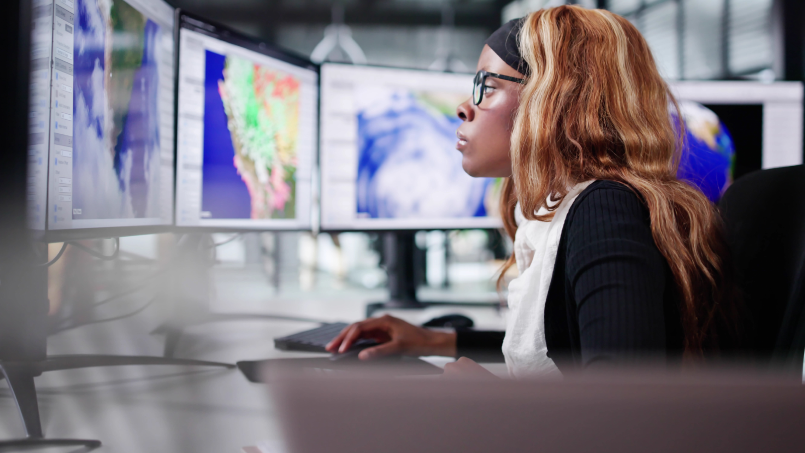 Vrouw achter computerschermen met beelden van het weer.
