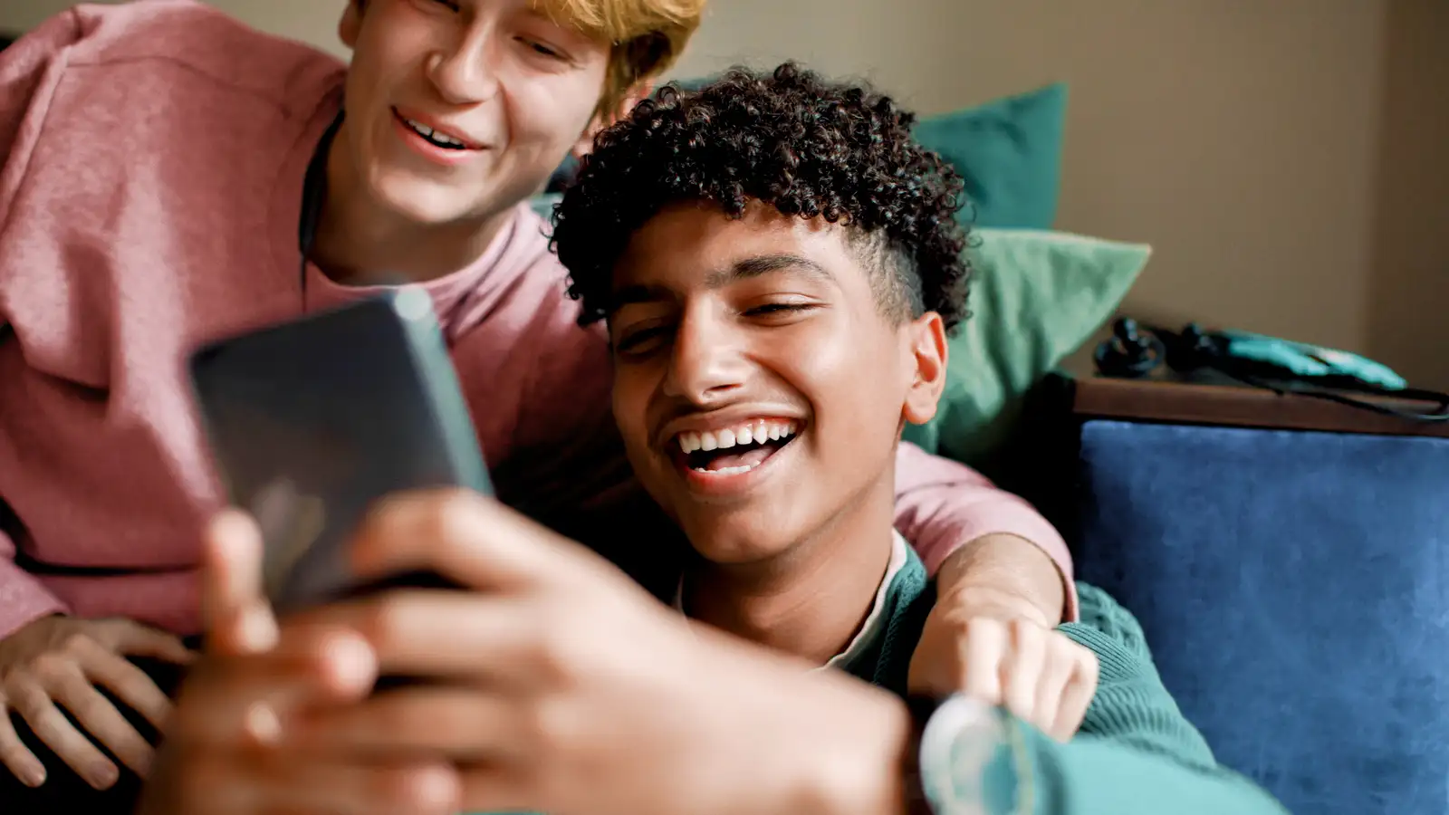 tieners lachend op de bank kijkend naar een telefoon