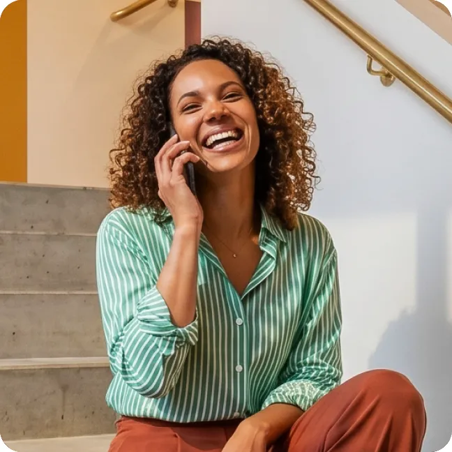 Glimlachende vrouw in een groen gestreept shirt tijdens een gesprek, zittend op een trap met een gouden leuning op de achtergrond.